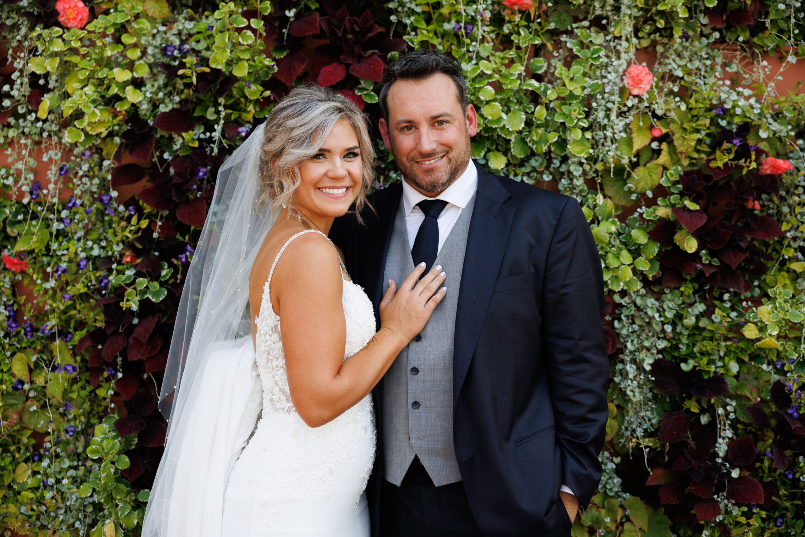 7N4A8025 A close-up of a bride and groom holding hands, showcasing their wedding bands and elegant attire against a softly lit background.