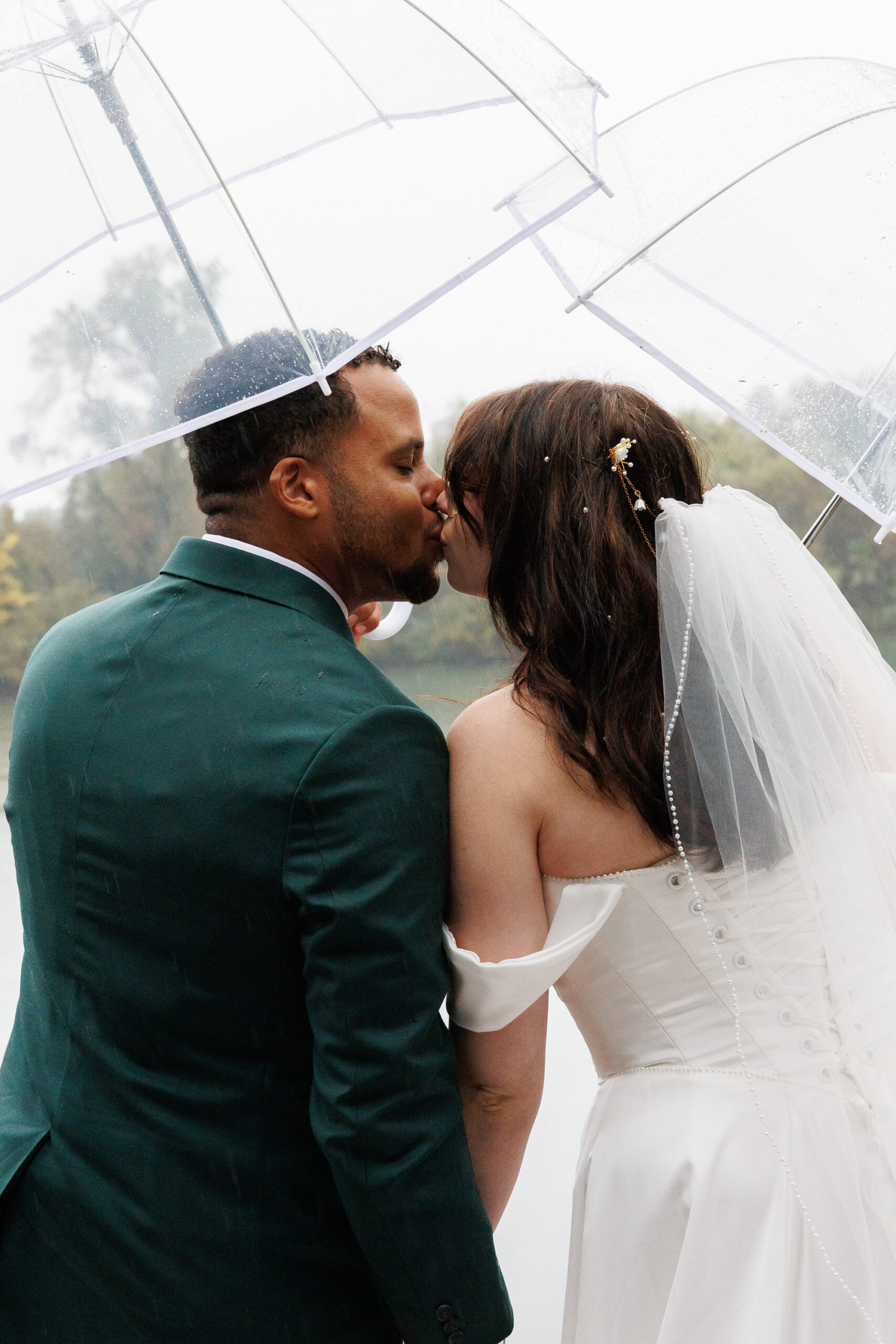 7N4A6451 A pregnant woman in a white lace dress cradles her baby bump while holding a vibrant sunflower surrounded by greenery.
